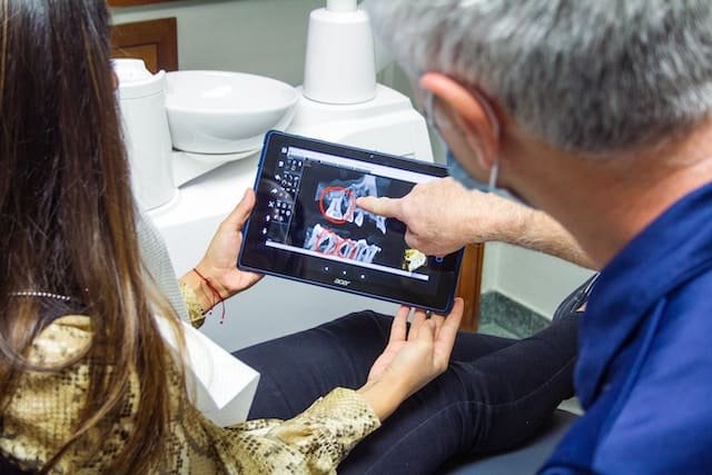 Ortodoncia en Costa Rica: Un doctor con una niña de paciente mostrándole una fotografía de su radiografía y apuntando hacia sus molares