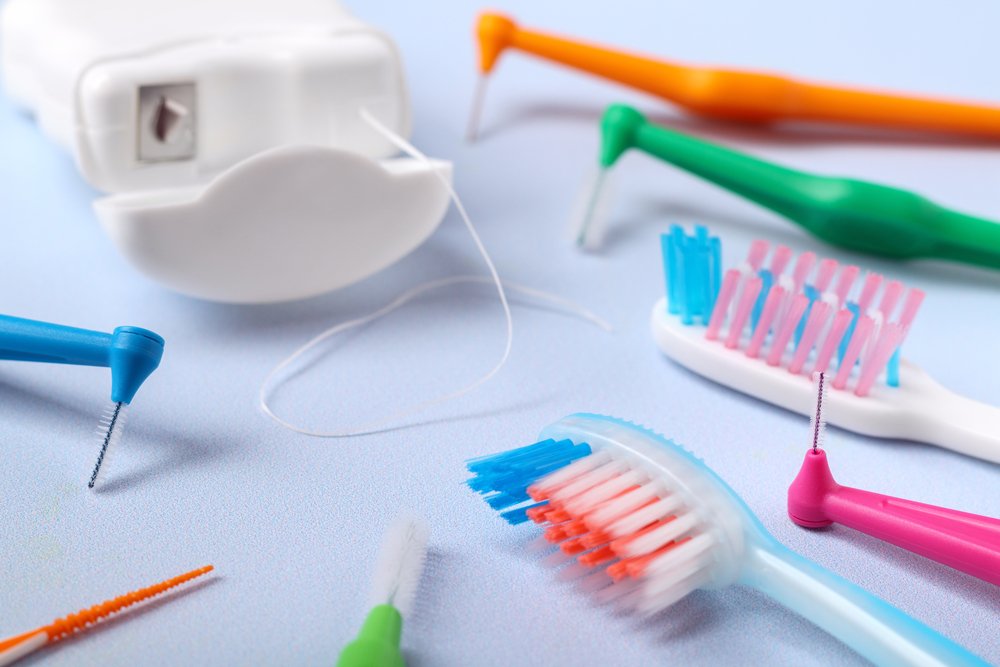 Cepillos dentales, hilo dental y cepillos interdentales bajo un fondo celeste claro para una buena limpieza dental con ortodoncia