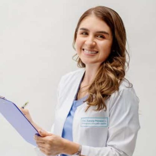 Dra. Natalia Morales sonriendo y haciendo apuntes bajo un fondo blanco